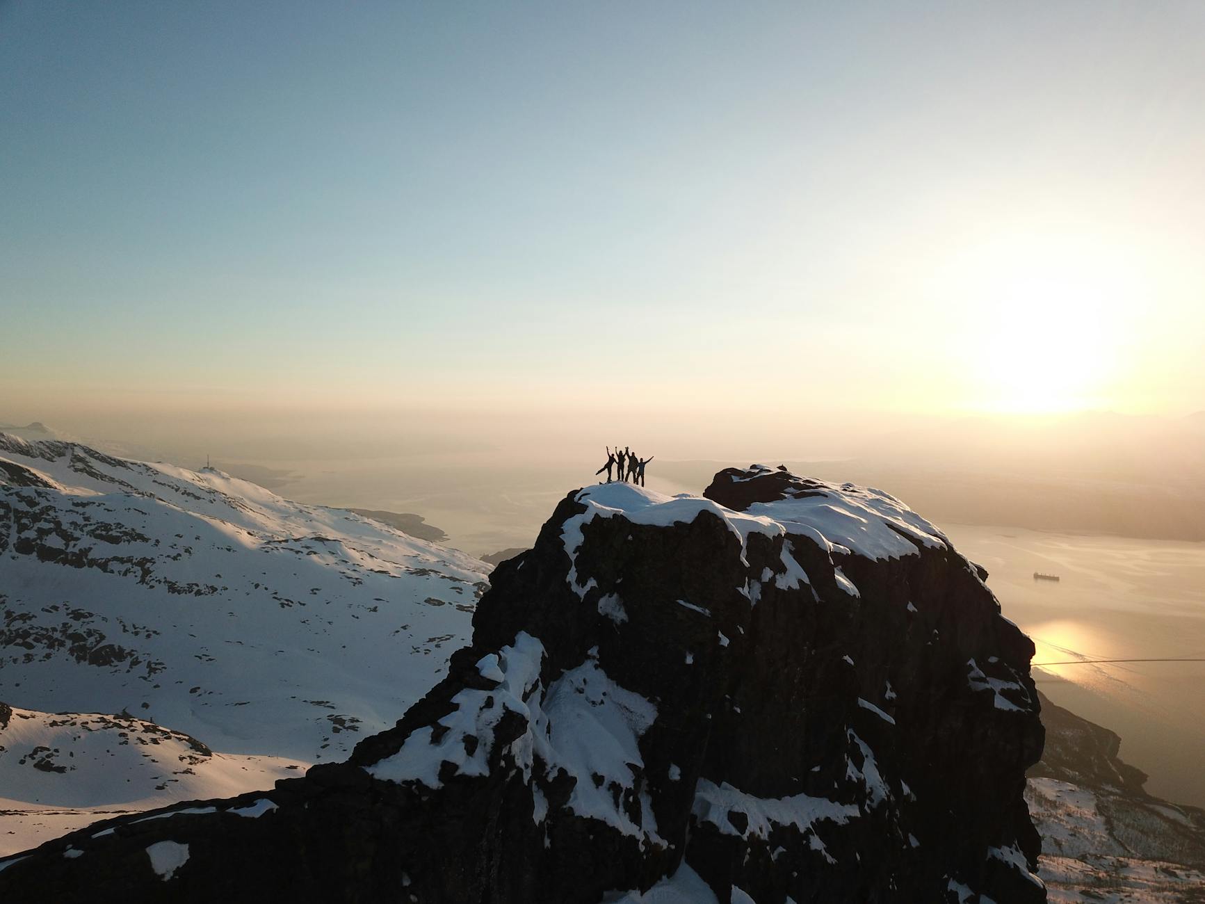 Adventurers celebrate atop a snow-covered peak in Narvik, Norway during sunrise.